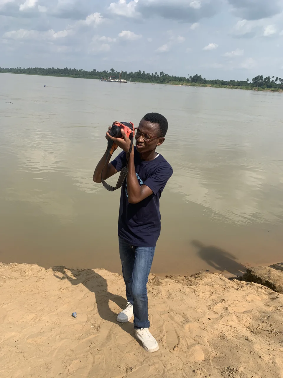 Divine using a camera beside a river.